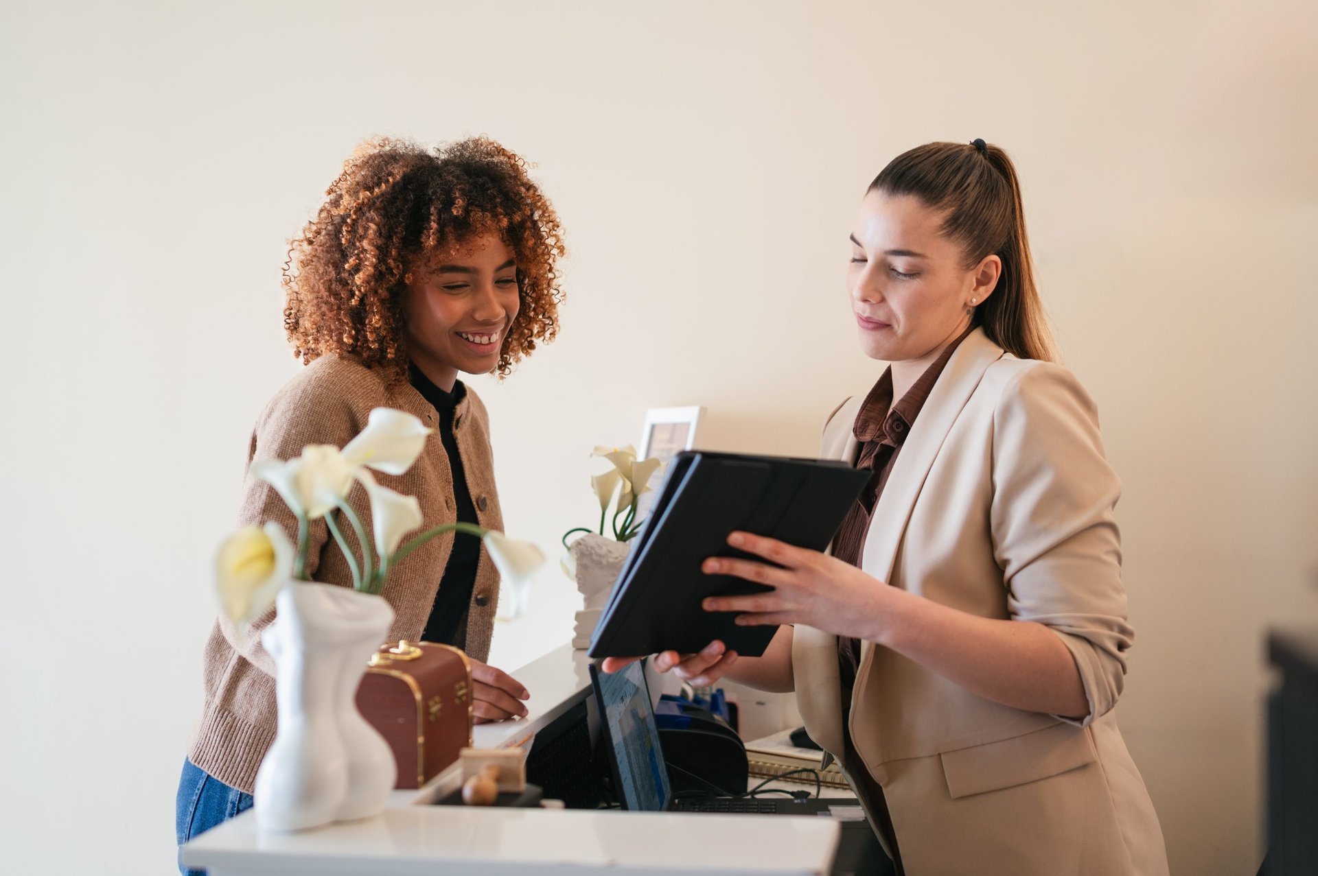Two women discussing services at a modern spa reception using a tablet